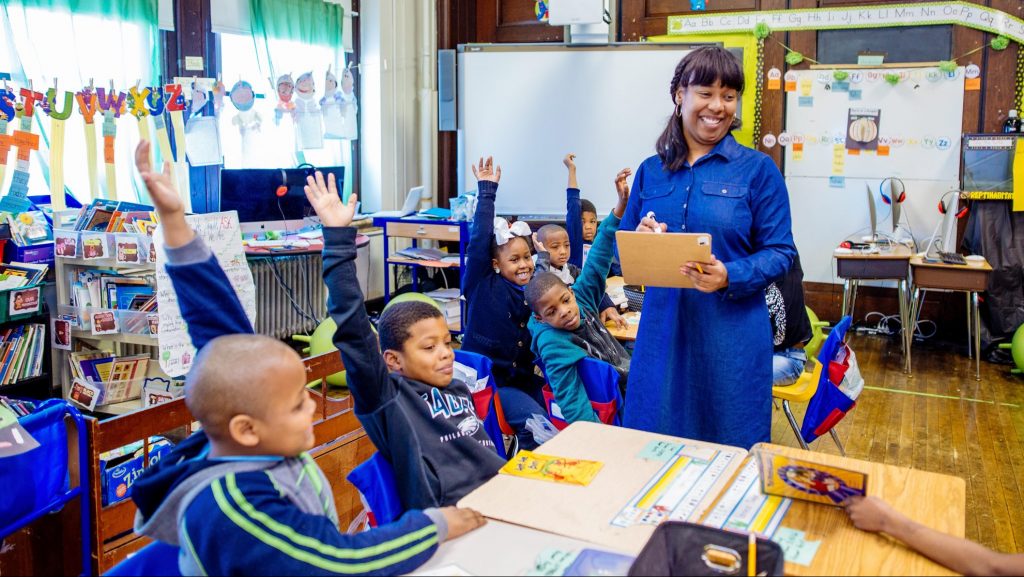 classroom; teacher; students with hands raised