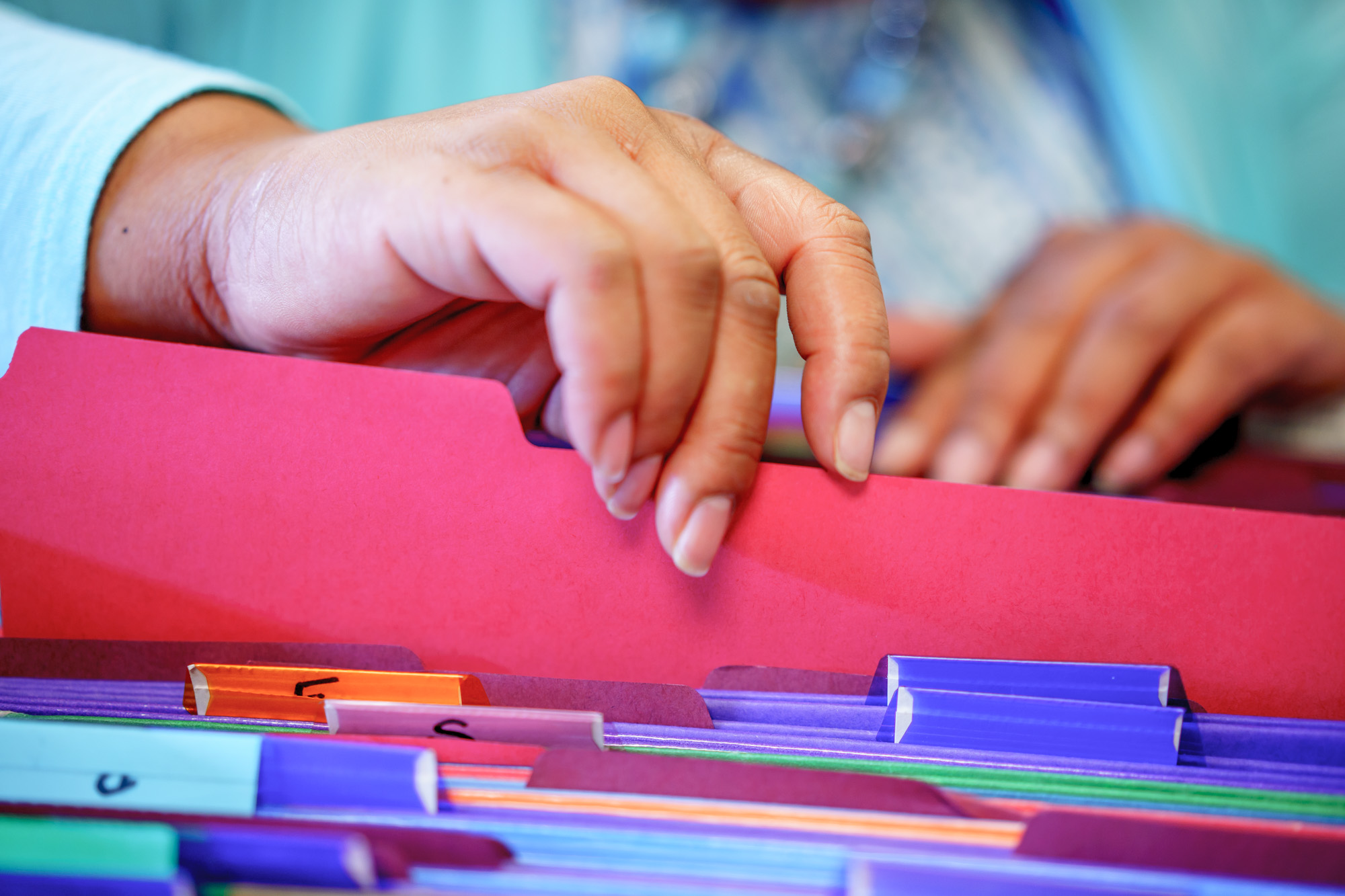 Hands flipping through file folders in a cabinet