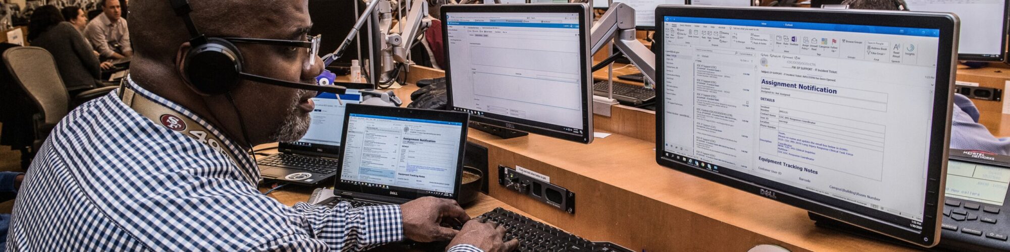 cdc-_XLJy3h77cw-unsplash and IT support technician is at his desk with many computer monitors as he takes in calls to assist people with IT problems
