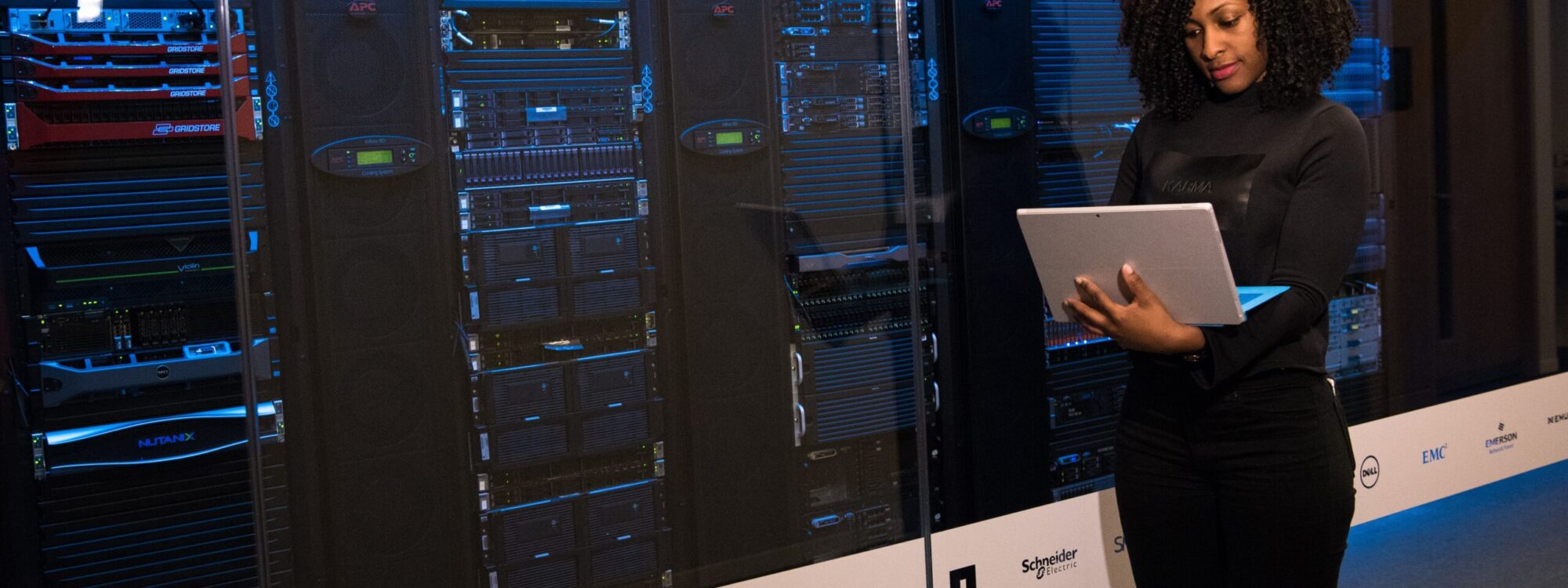 pexels-christina-morillo-1181354 woman holding laptop is in front of a wall of server machines