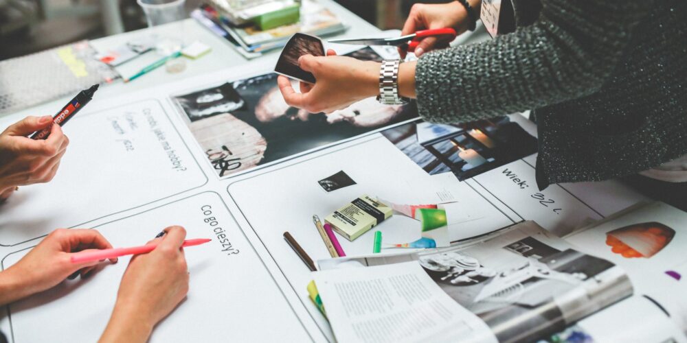 pexels-kaboompics-com-6224 graphic designers gather around printed material to discuss layouts, proofs, and colors