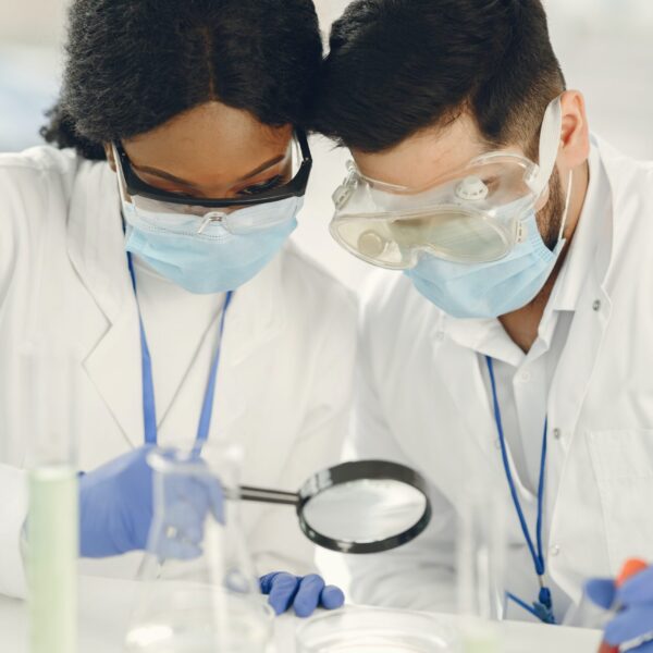two lab scientists inspect a petri dish with a magnifying glass