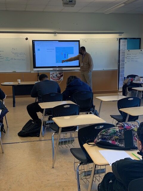 Reggie Moton standing in front of a classroom to teach content shown on a smart board
