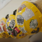 A row of yellow construction hats hang on the wall of a Mayfair clasroom, where they are exposing middle school students to building trades.