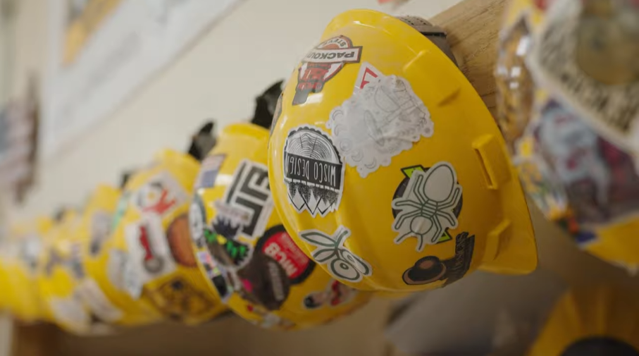 A row of yellow construction hats hang on the wall of a Mayfair clasroom, where they are exposing middle school students to building trades.