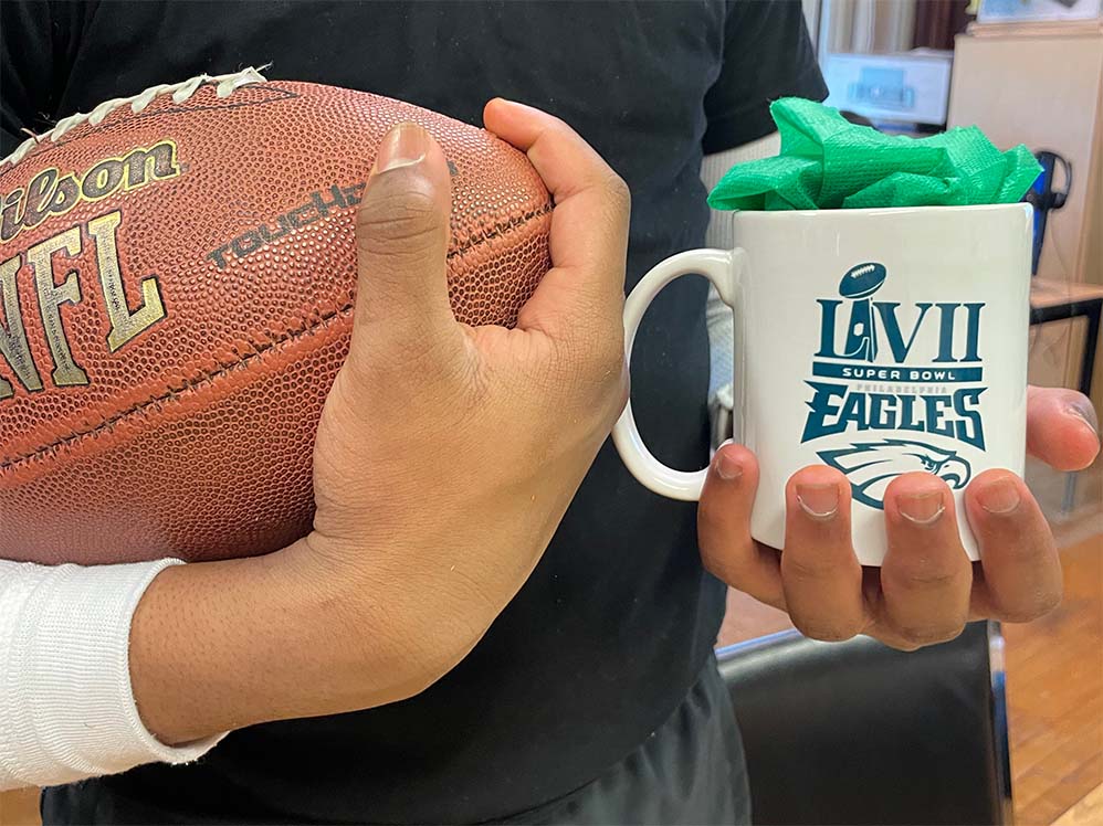 cropped photo of a high school student holding one of the Eagles mugs in one hand and an NFL football in the other