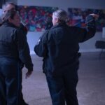 A candid photo taken during KCAPA's "Story Time" art exhibit. A group of three police officers are conversing with their backs turned to the camera. The background shows two artworks that look like mosaics.