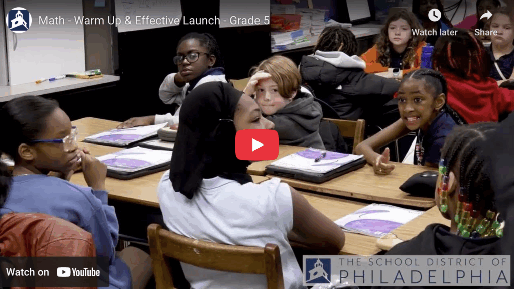 Teacher at board writing answers as children raise their hands