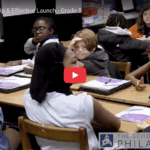 Teacher at board writing answers as children raise their hands