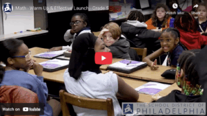 Teacher at board writing answers as children raise their hands