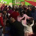 Several young female students dance with their fathers in a school gymnasium with green walls and red ribbon hanging.