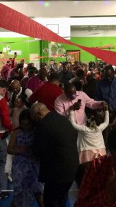 Several young female students dance with their fathers in a school gymnasium with green walls and red ribbon hanging.