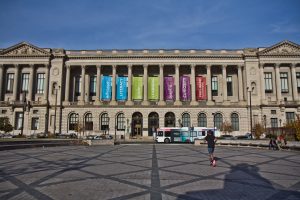 Facade of Free Library of Philadelphia on Vine Street, with runner in foreground. Library has large columns with colorful banners between them.