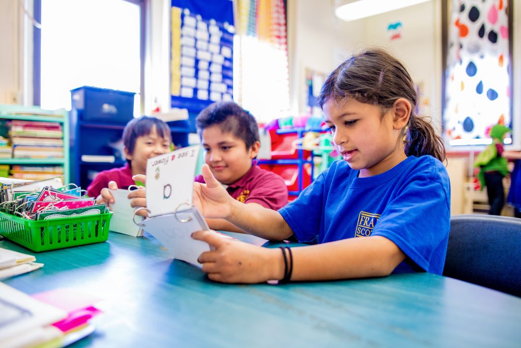 Three children sitting at a desk using flash cards.