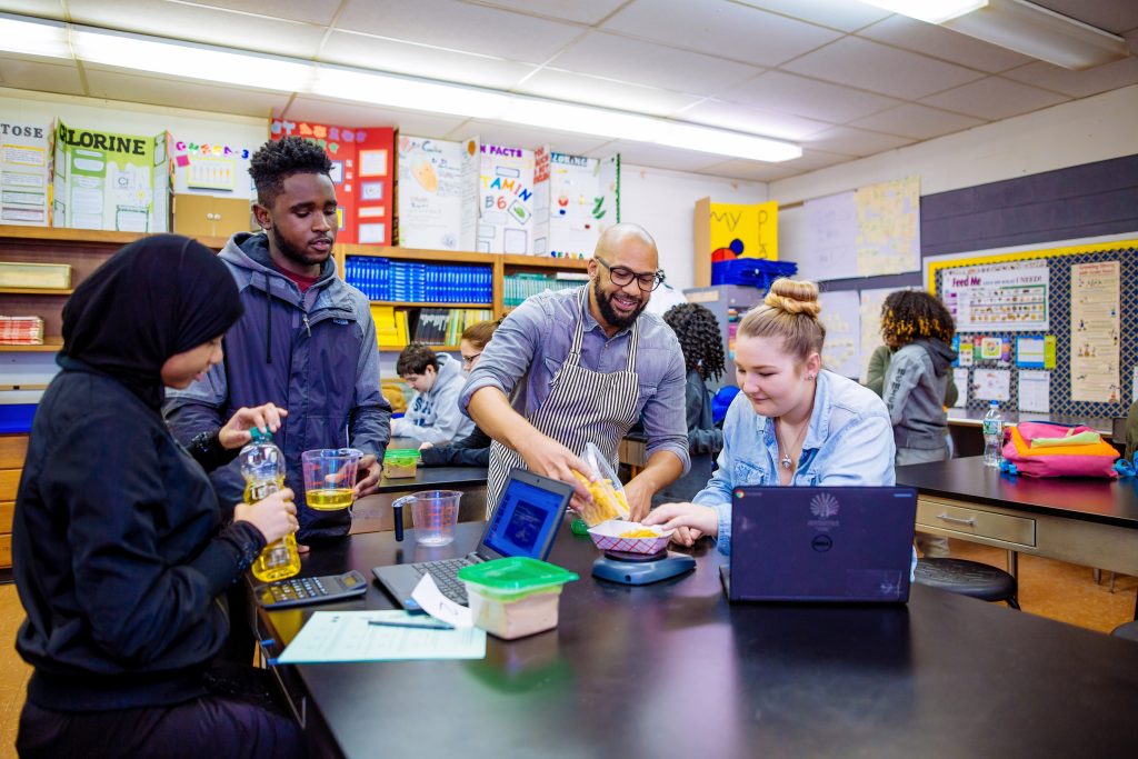 Male science teacher working with three students on experiment