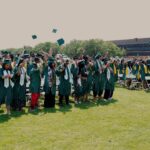 Graduates in a field throwing their caps in the air after the ceremony