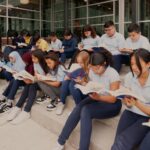 A classroom of students is sitting on the steps outside of school and reading.