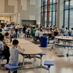 Wide shot of elementary students eating in a cafeteria with windows