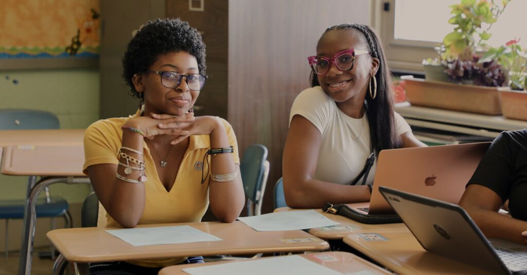 Two SDP high school students sitting at desks and smiling at the camera