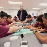 Middle school students around a table working eagerly on a math project, with their teacher encouraging them