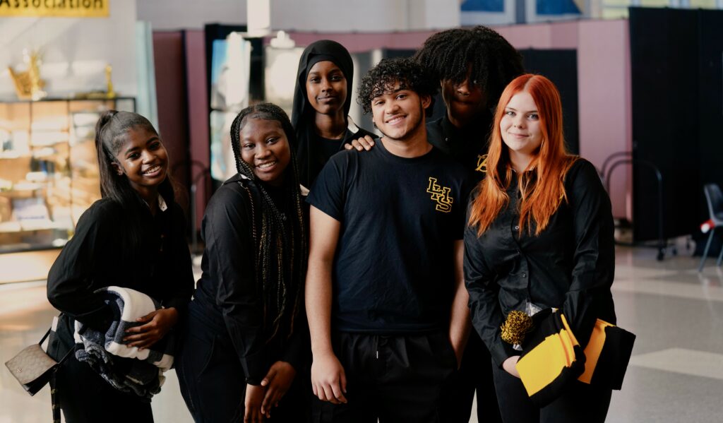 Diverse group of 6 high schoolers in black uniforms smiling together for the camera