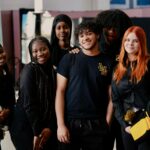 Diverse group of 6 high schoolers in black uniforms smiling together for the camera
