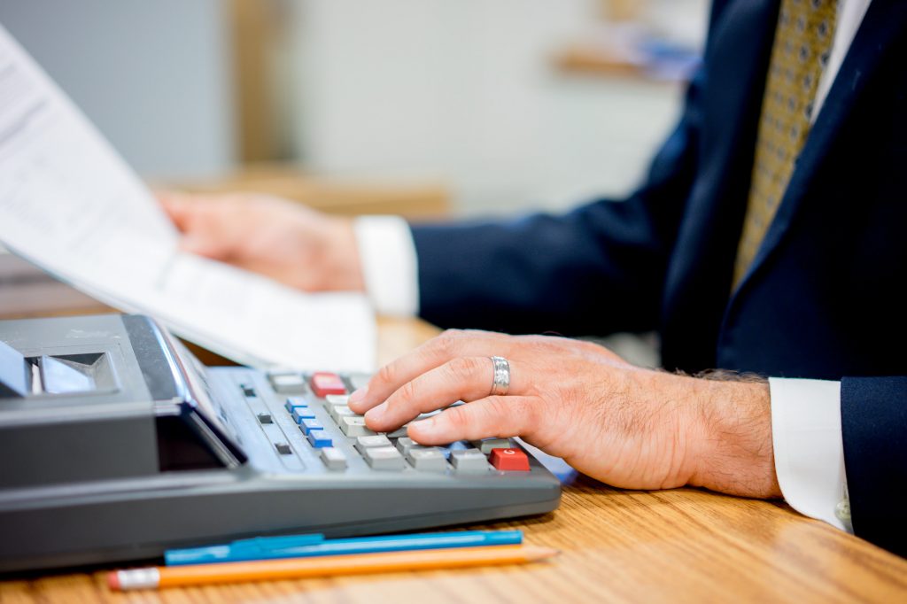 A man's hand typing on a calculator