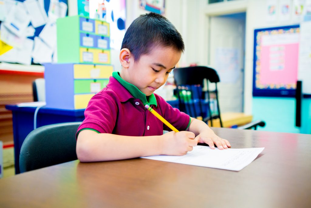 A student is writing on a piece of paper with a pencil