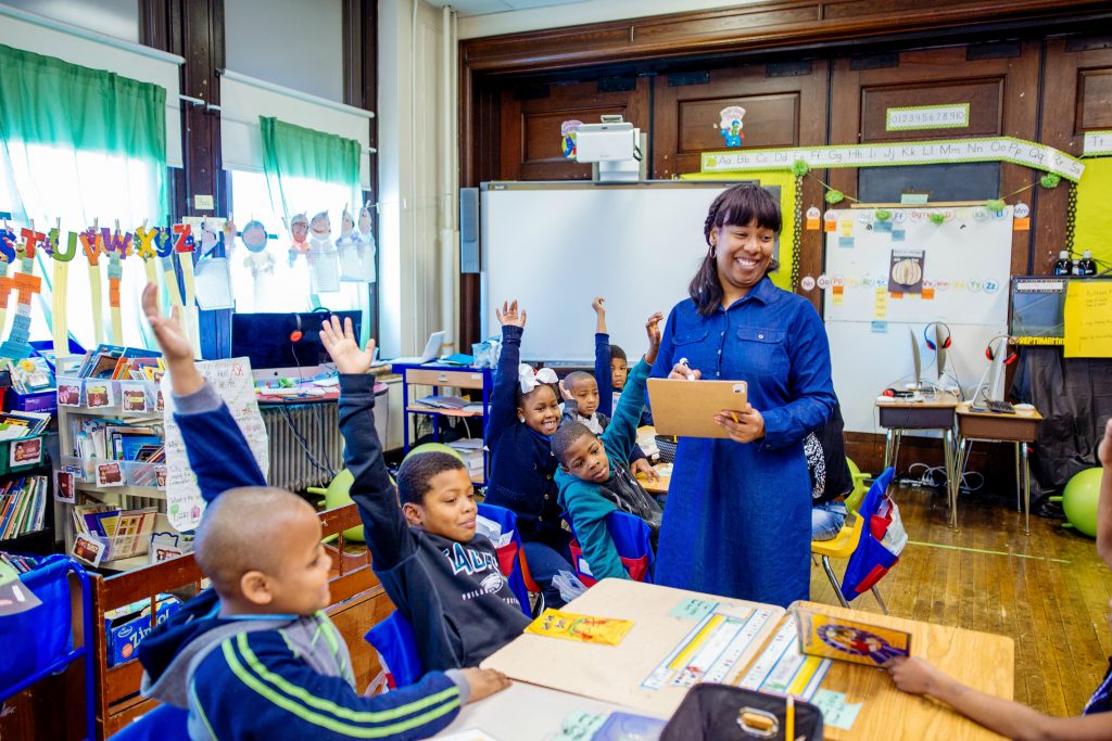 Kids in a classroom raising their hands and participating in class.