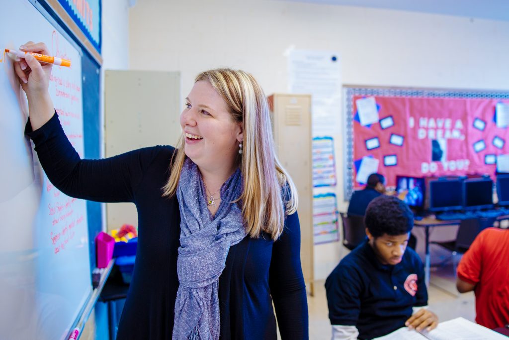 A teacher is writing on the board in front of her class.