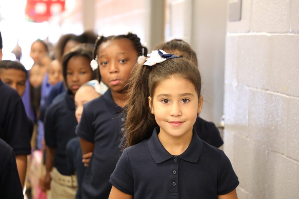 smiling elementary age student in front of a line of students in hallway