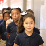 smiling elementary age student in front of a line of students in hallway