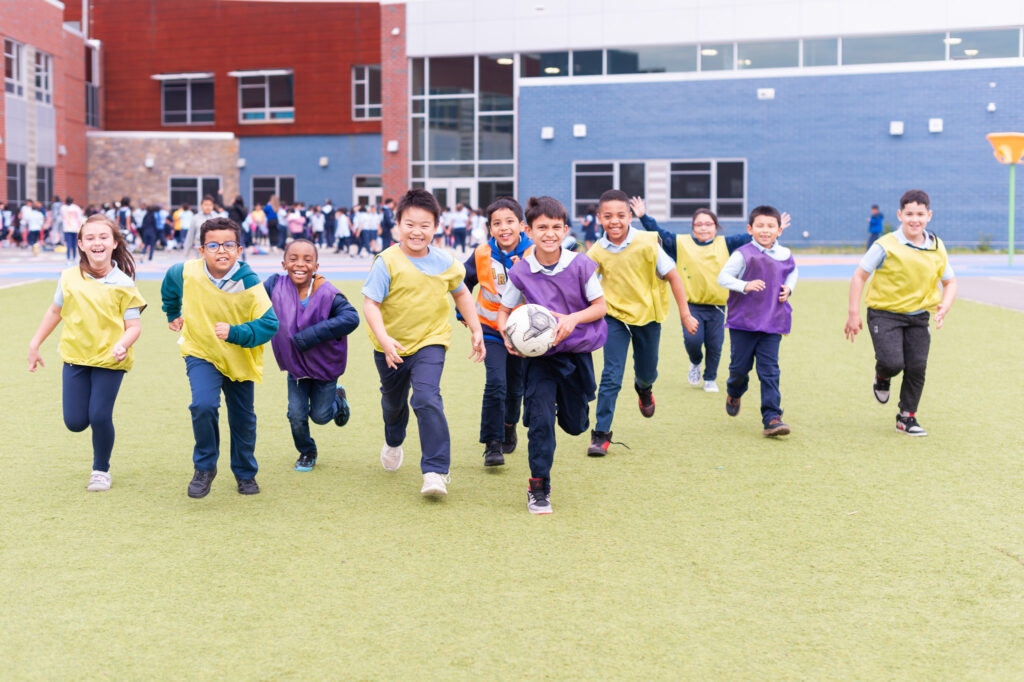 Students running and smiling with a soccer ball