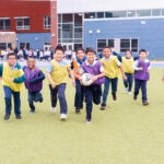 Students running and smiling with a soccer ball