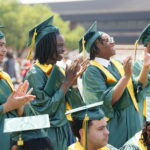 Four prominent graduating seniors standing and clapping in caps and gown