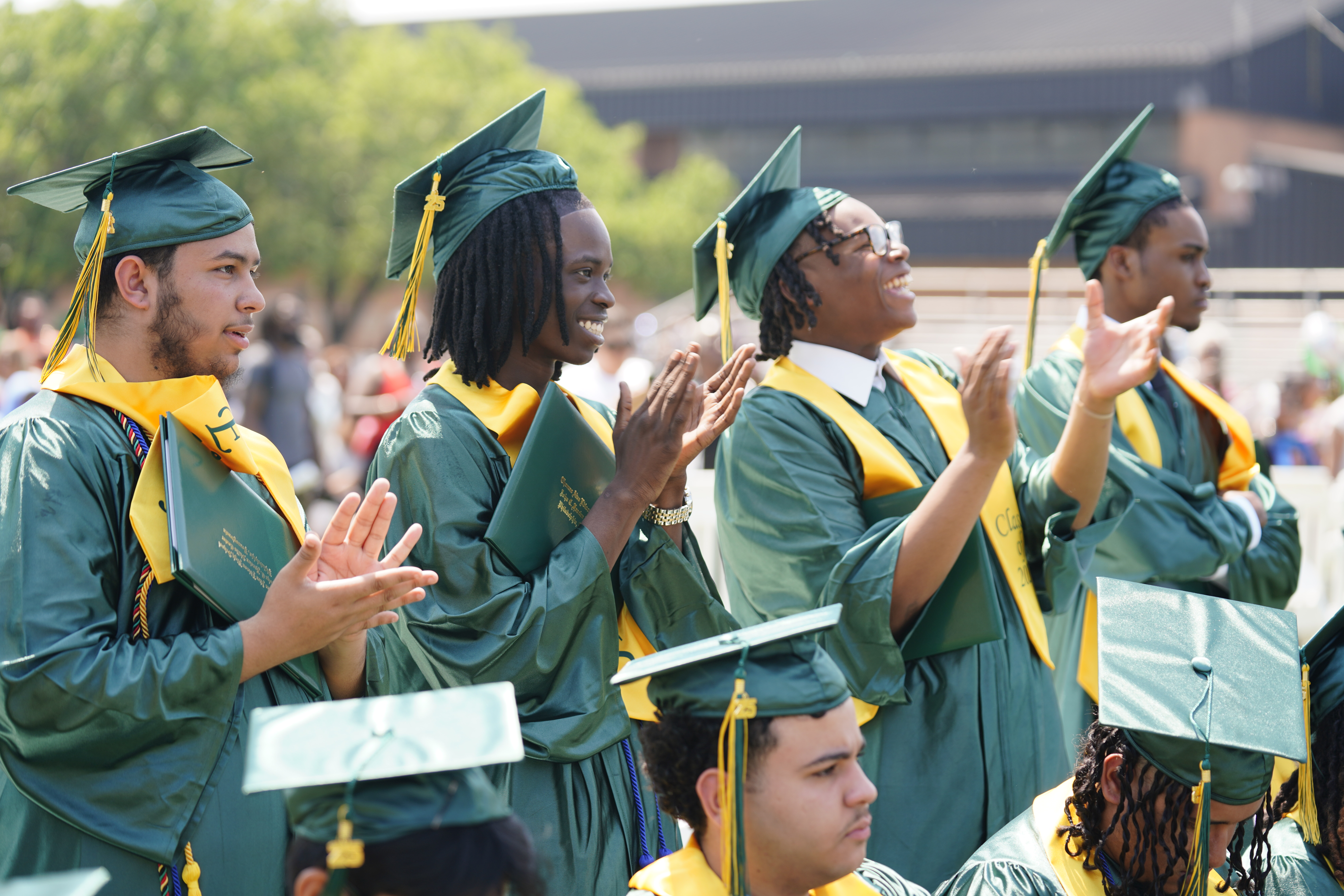 Four prominent graduating seniors standing and clapping in caps and gown