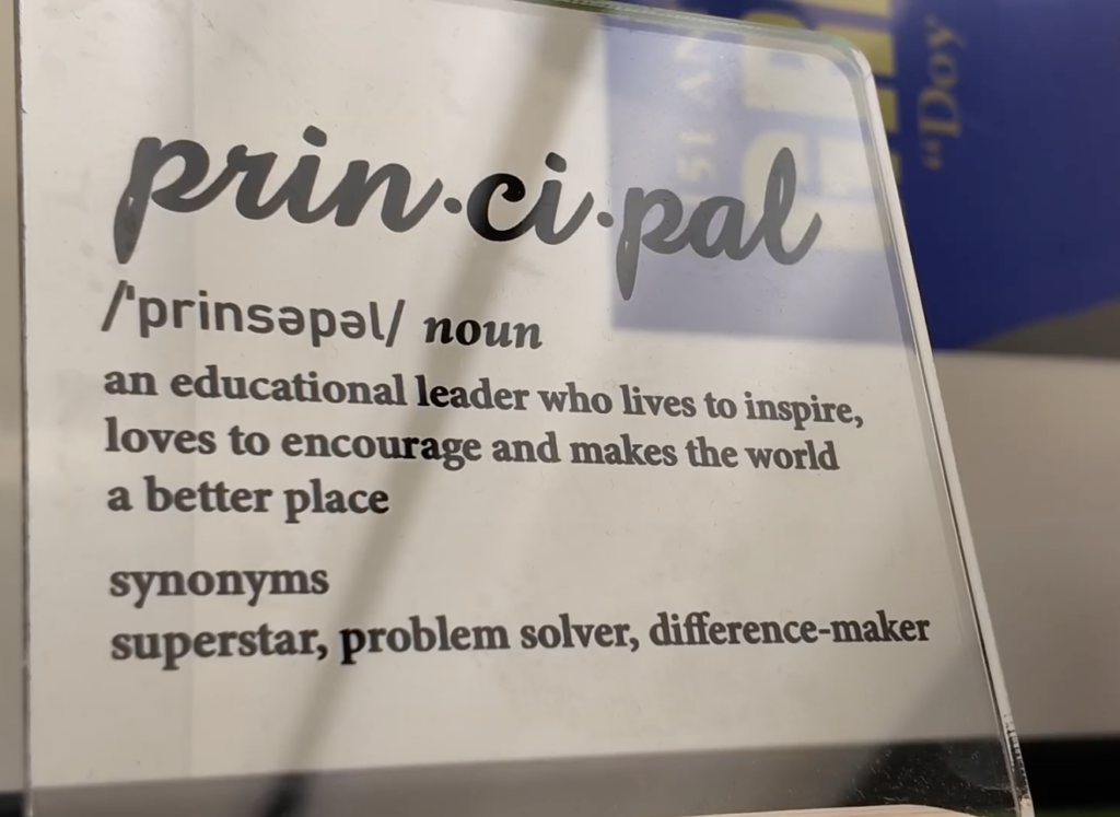Plaque defining a principal as “an educational leader who lives to inspire, loves to encourage and makes the world a better place.” Synonyms listed: superstar, problem solver, difference-maker.